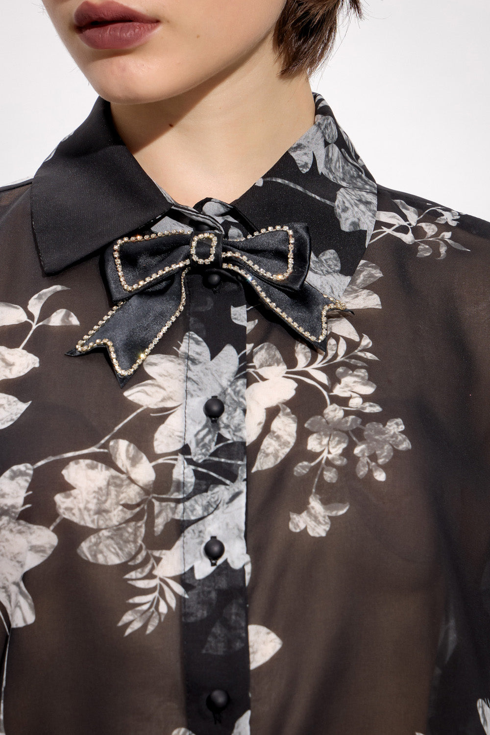 Γυναικεία μαύρη φλοράλ πουκαμίσα με διακοσμητικό φιόγκο και μακριά μανίκια, φορεμένη με μαύρο παντελόνι.