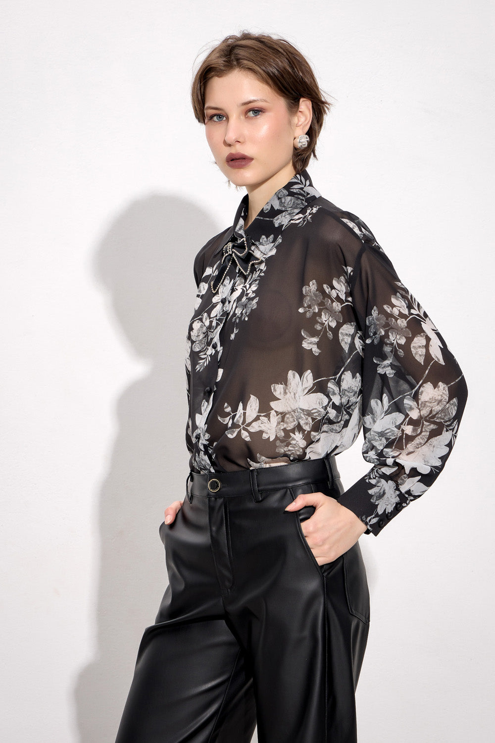 Γυναικεία μαύρη φλοράλ πουκαμίσα με διακοσμητικό φιόγκο και μακριά μανίκια, φορεμένη με μαύρο παντελόνι.