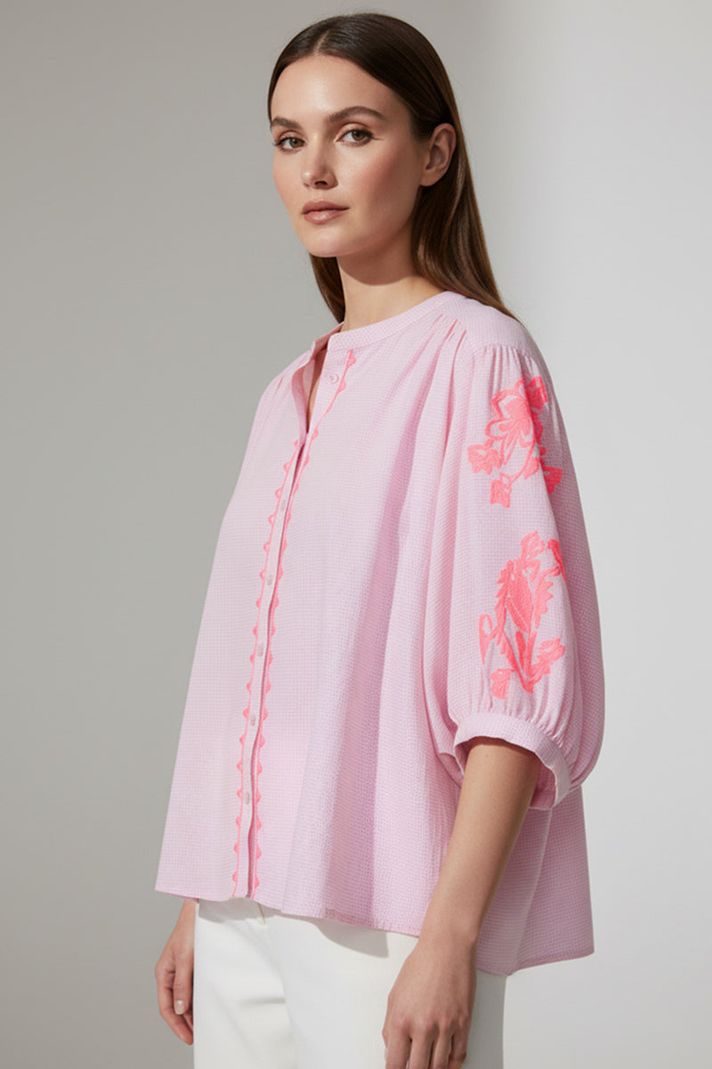Γυναικείο ροζ πουκάμισο με κεντημένες λεπτομέρειες στα μανίκια και χαλαρή γραμμή, φορεμένο με λευκό παντελόνι.