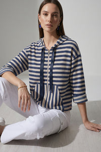 Γυναικεία ριγέ ζακέτα με κουκούλα και φερμουάρ σε μπλε και εκρού αποχρώσεις, φορεμένη με λευκό cargo παντελόνι.