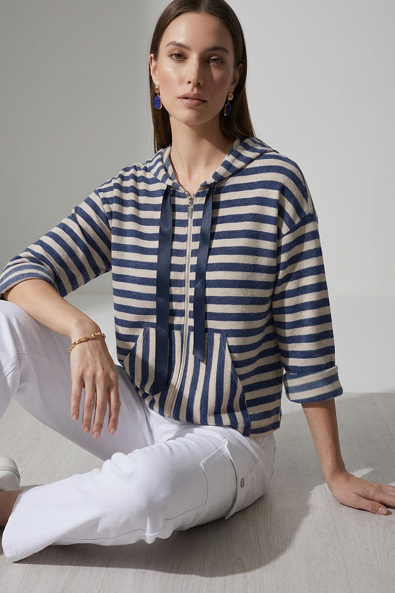 Γυναικεία ριγέ ζακέτα με κουκούλα και φερμουάρ σε μπλε και εκρού αποχρώσεις, φορεμένη με λευκό cargo παντελόνι.