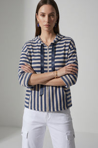 Γυναικεία ριγέ ζακέτα με κουκούλα και φερμουάρ σε μπλε και εκρού αποχρώσεις, φορεμένη με λευκό cargo παντελόνι.