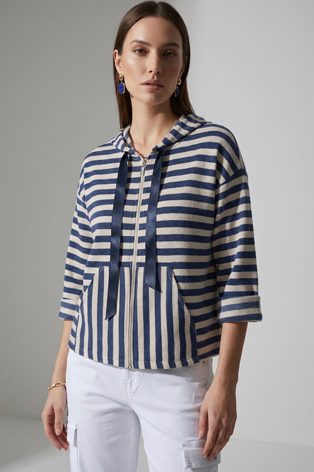 Γυναικεία ριγέ ζακέτα με κουκούλα και φερμουάρ σε μπλε και εκρού αποχρώσεις, φορεμένη με λευκό cargo παντελόνι.