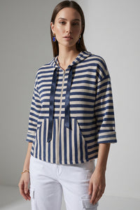 Γυναικεία ριγέ ζακέτα με κουκούλα και φερμουάρ σε μπλε και εκρού αποχρώσεις, φορεμένη με λευκό cargo παντελόνι.