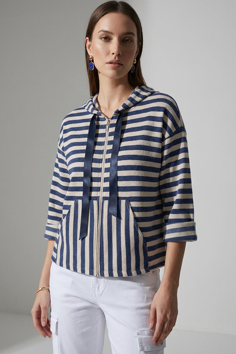 Γυναικεία ριγέ ζακέτα με κουκούλα και φερμουάρ σε μπλε και εκρού αποχρώσεις, φορεμένη με λευκό cargo παντελόνι.