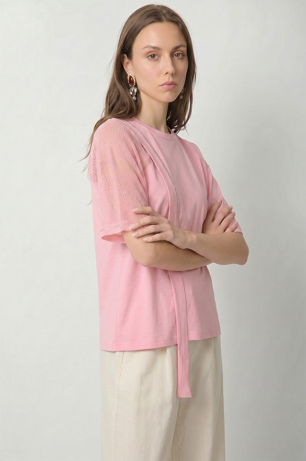 Ροζ γυναικείο T-shirt με διαφανές μανίκι, ανάγλυφο λεκτικό σχέδιο και διακοσμητική κάθετη κορδέλα στο μπροστινό μέρος.