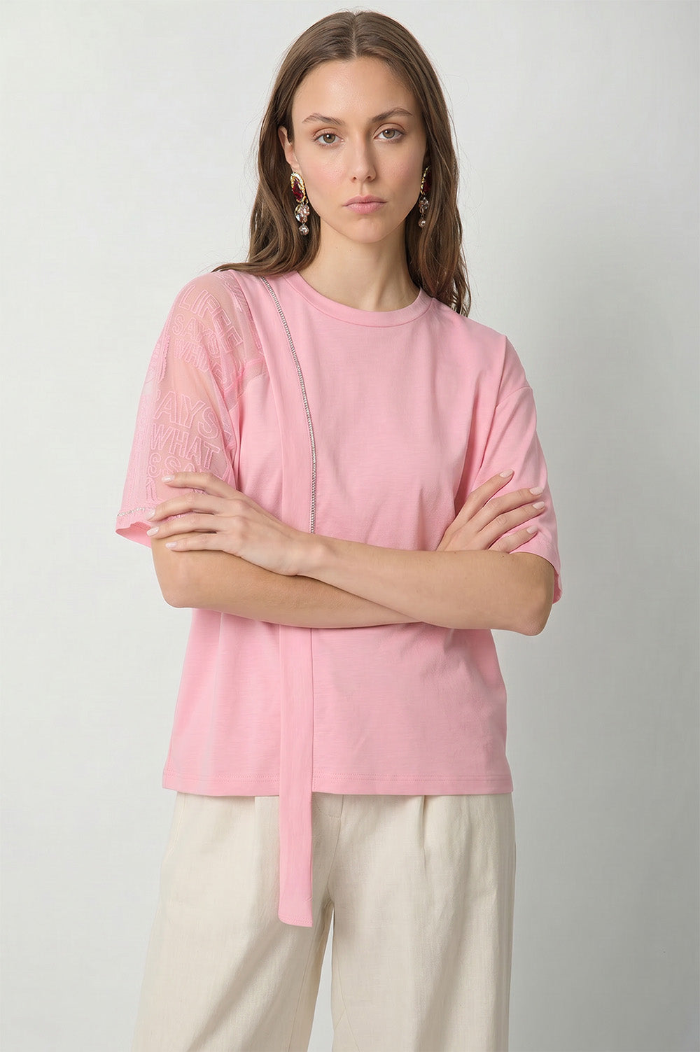 Ροζ γυναικείο T-shirt με διαφανές μανίκι, ανάγλυφο λεκτικό σχέδιο και διακοσμητική κάθετη κορδέλα στο μπροστινό μέρος.