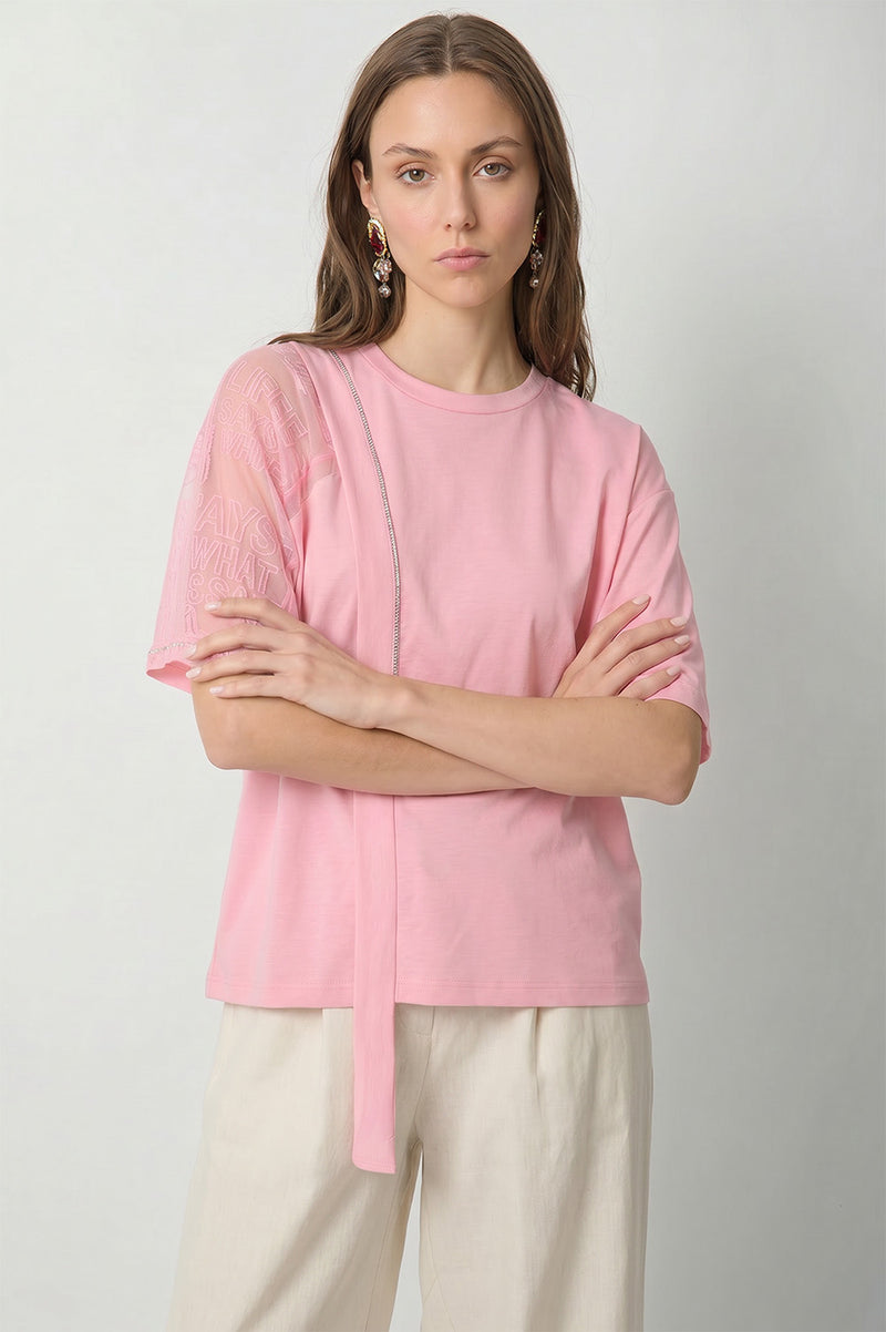 Ροζ γυναικείο T-shirt με διαφανές μανίκι, ανάγλυφο λεκτικό σχέδιο και διακοσμητική κάθετη κορδέλα στο μπροστινό μέρος.