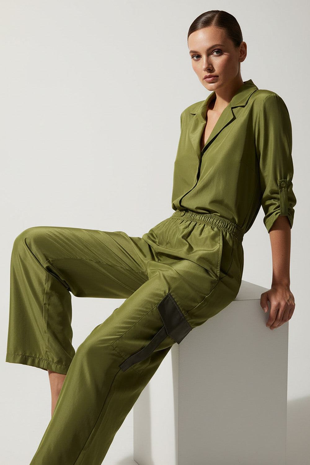 Πράσινη σατέν ολόσωμη φόρμα με ελαστική μέση και cargo λεπτομέρειες σε στούντιο φωτογράφιση.