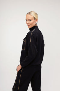 Μαύρο γυναικείο σετ με χρυσή ρέλι, μπλούζα με φερμουάρ και ίσιο παντελόνι σε άνετη γραμμή.