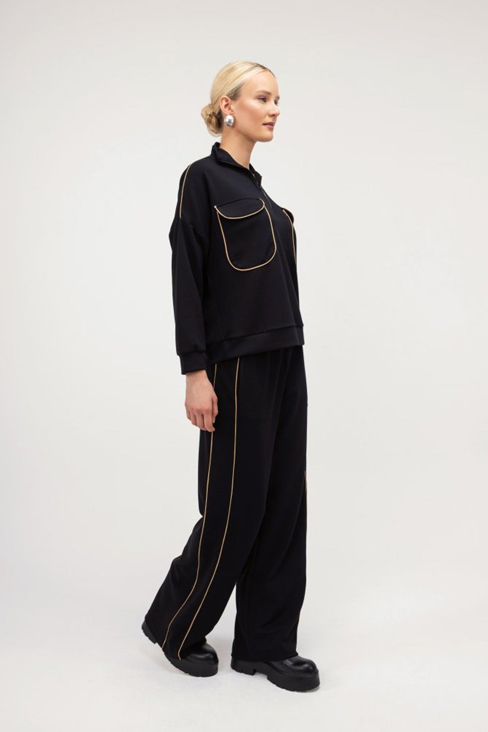 Μαύρο γυναικείο σετ με χρυσή ρέλι, μπλούζα με φερμουάρ και ίσιο παντελόνι σε άνετη γραμμή.