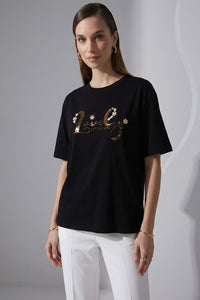 Γυναικείο μαύρο t-shirt με κεντημένο λογότυπο και διακοσμητικές χάντρες, φορεμένο με λευκό παντελόνι.