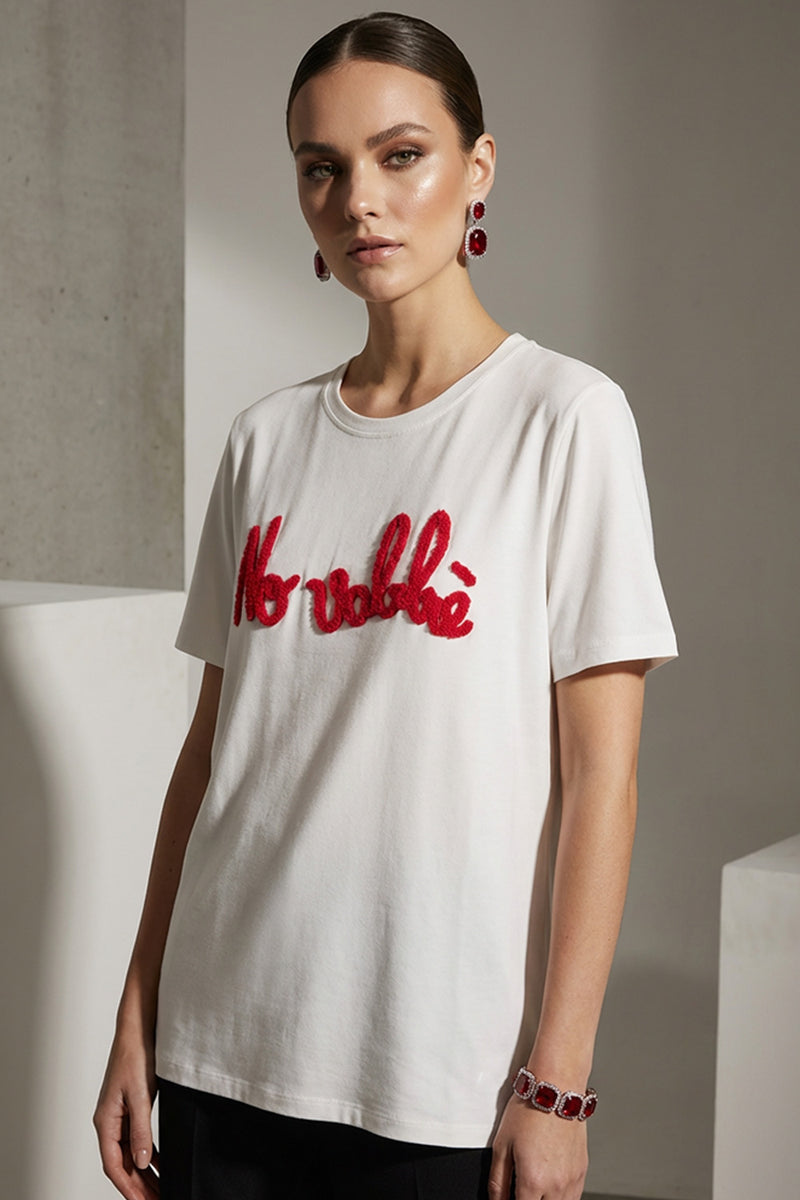 Γυναικείο λευκό t-shirt με κόκκινο κεντημένο μήνυμα και κοντό μανίκι, φορεμένο με μαύρο παντελόνι.