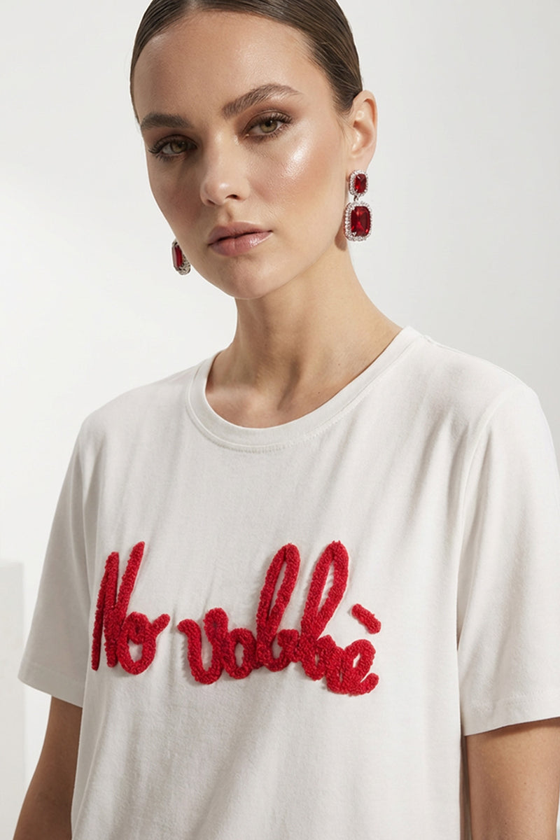 Γυναικείο λευκό t-shirt με κόκκινο κεντημένο μήνυμα και κοντό μανίκι, φορεμένο με μαύρο παντελόνι.