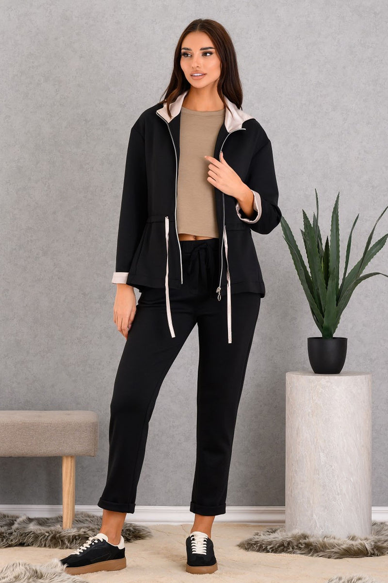 Woman wearing a black outfit with beige top in a room with a gray wall and plant.